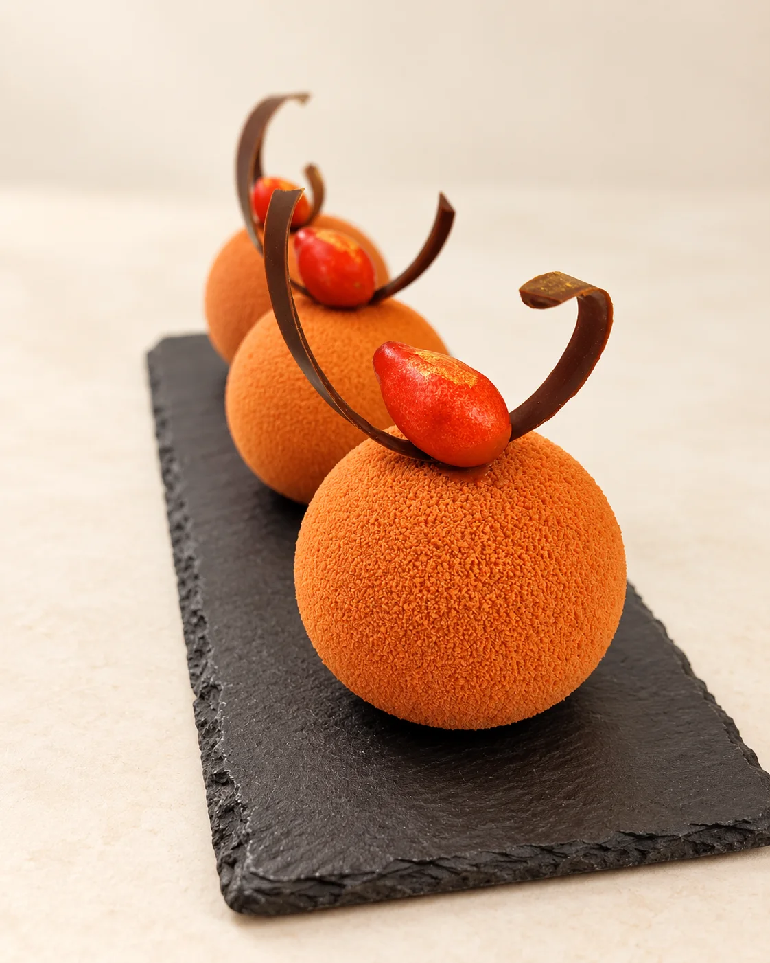 Zwei runde orangefarbene Desserts mit Schokoladendekor